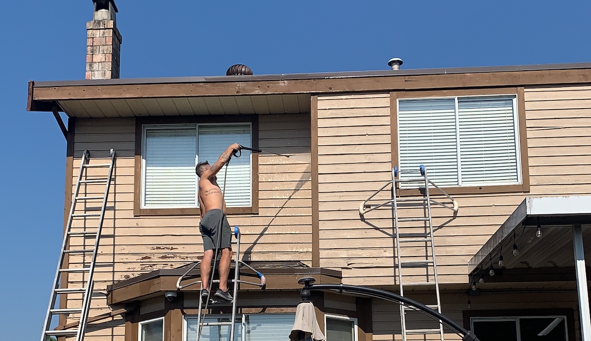 A professional painting contractor working on a two-story suburban house in Coquitlam