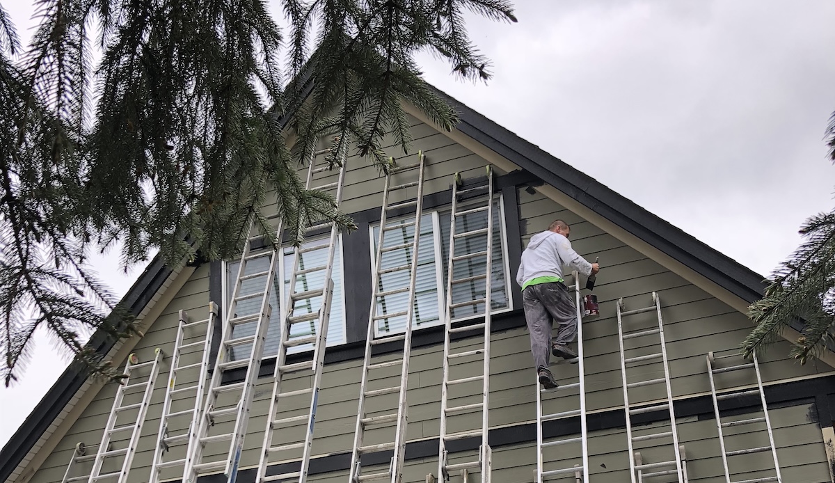 A skilled painter in a white uniform applies fresh paint to the exterior of a modern home in Coquitlam, British Columbia